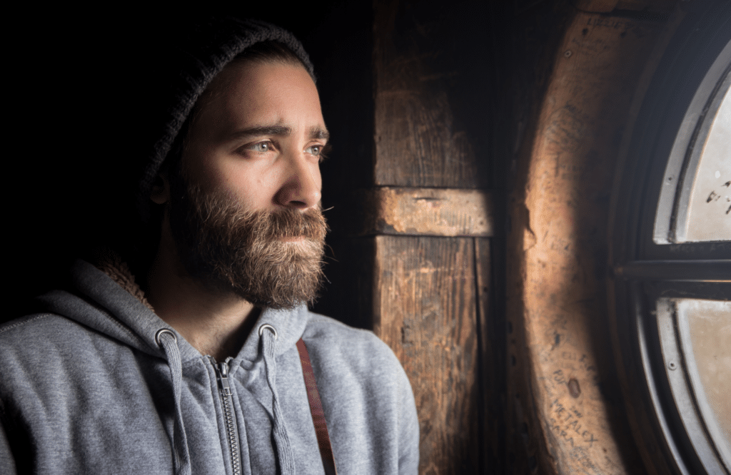 man in a grey hoodie looking out a window