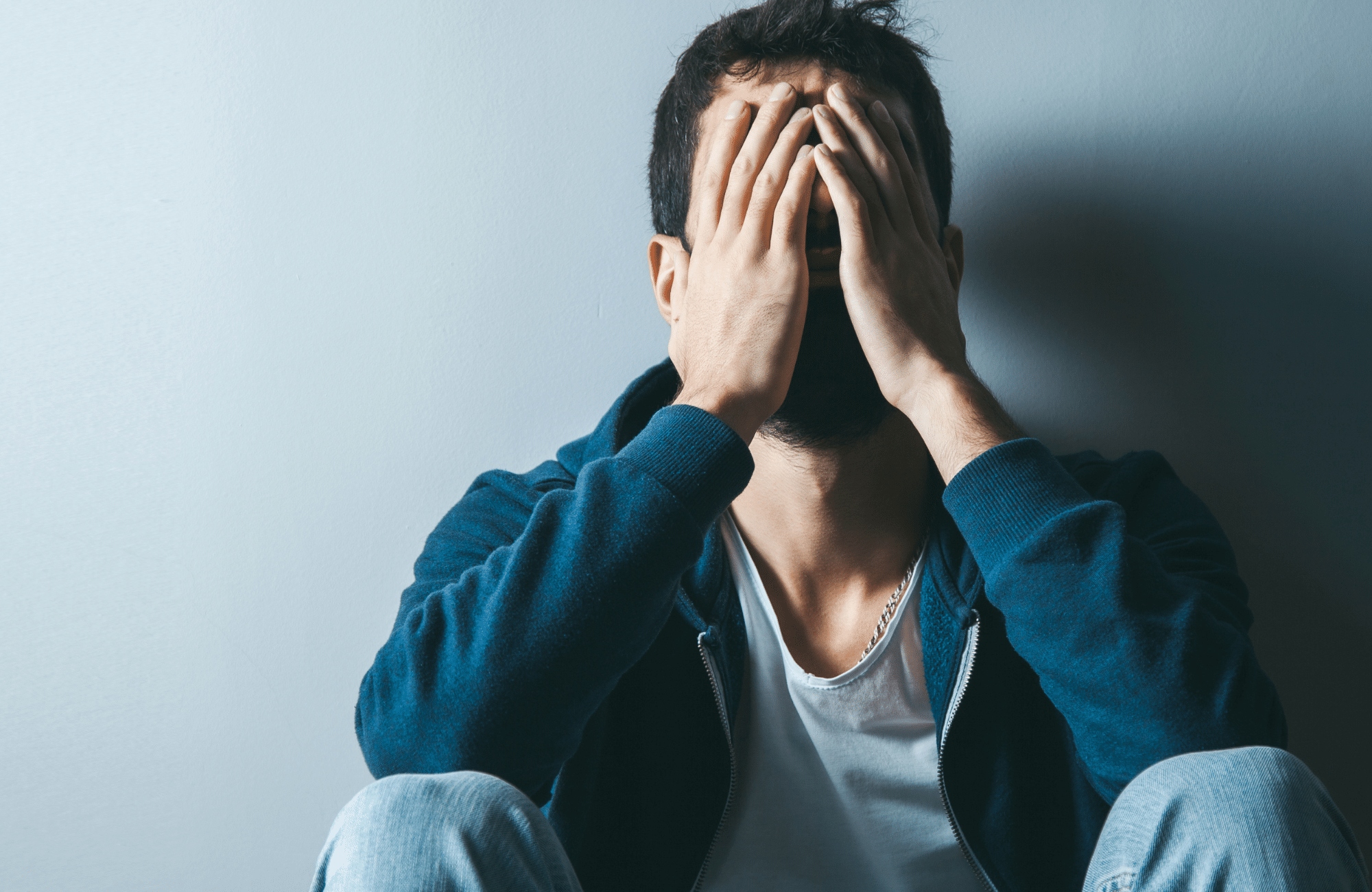 Image of a man in a blue sweater covering his face. Representing how loss can feel without the support of a grief counsellor in Sherwood Park, AB. Loss is difficult but with grief counselling in Edmonton, AB can bring hope back in your life